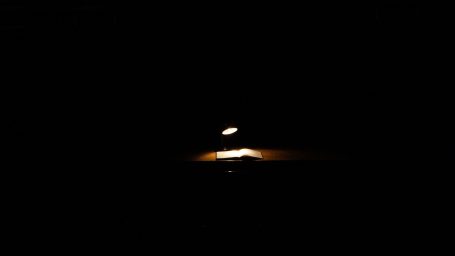 Schreibtisch mit einer einzelnen Schreibtischlampe, die ein offenes Buch beleuchtet