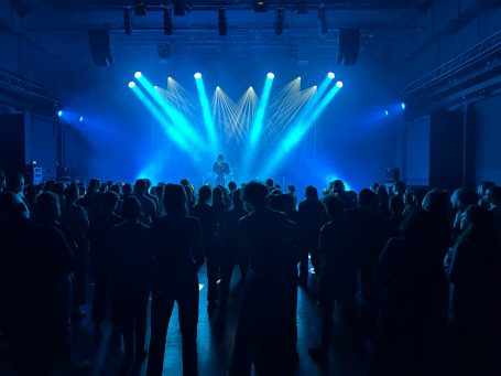 Ein Konzertausschnitt mit einer Menschenmenge und blauen Lichtstrahlen auf der Bühne.