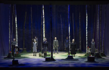 Theateraufführung in einem Wald mit sieben Darstellern zwischen Bäumen.