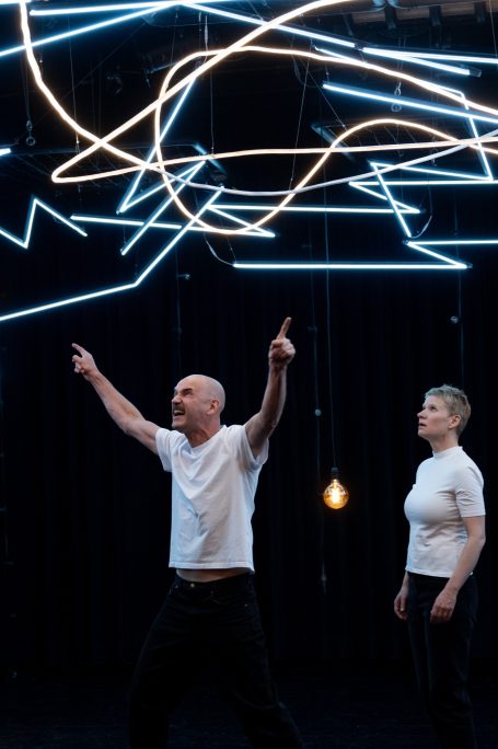 Zwei Tänzer auf einer Bühne mit leuchtenden Linien im Hintergrund.