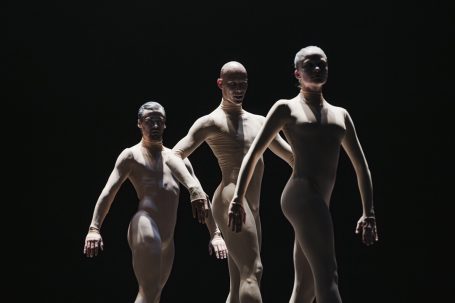 Drei stilisierte, menschliche Figuren stehen in einer dunklen Umgebung.