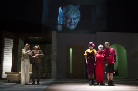 Szenen aus einem Theaterstück mit Schauspielern und einer Projektion eines bedrohlichen Gesichts.