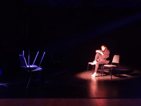 Ein einzelner Mensch sitzt auf einem Stuhl in einem dunklen Raum mit schwachem Licht.