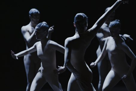 Fünf silhouettenhafte Tänzer in ausdrucksvoller Pose vor schwarzem Hintergrund.