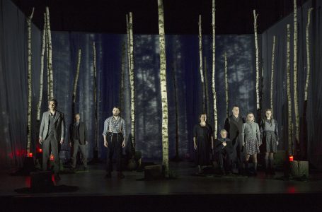 Szenenbild mit mehreren Personen in einem Waldbereich mit Birkenstämmen.